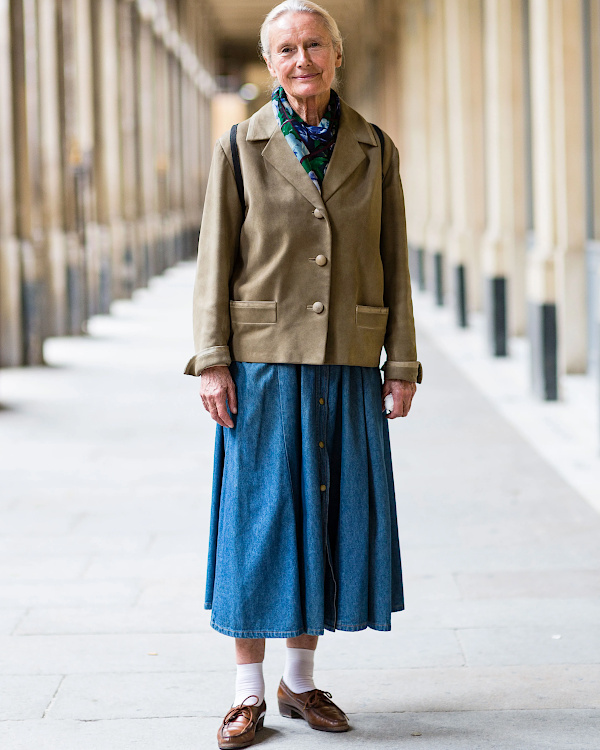 Femme de 70 ans portant un manteau rose vif, une jupe midi fluide et des chaussures claires au printemps