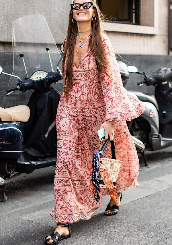 Femme portant une robe longue imprimée rose et rouge avec des sandales noires dans une rue urbaine
