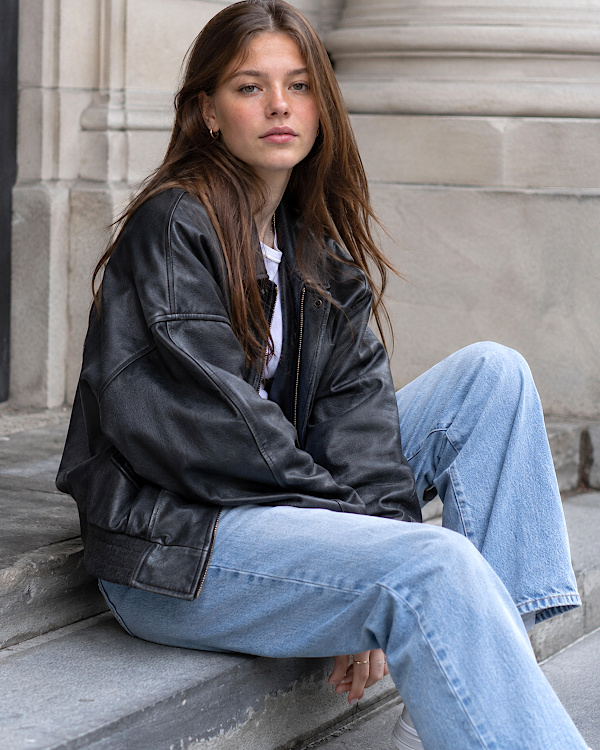 Femme brune en veste en cuir noir et jean large bleu clair