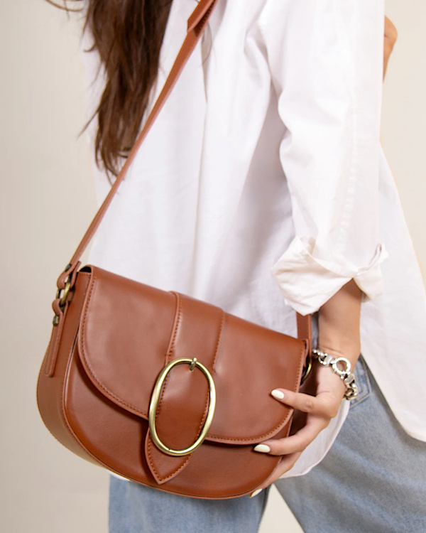 Sac bandoulière en cuir cognac porté avec une chemise blanche et un jean
